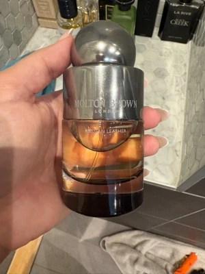 Molton Brown Russian Leather parfym - Molton Brown Russian Leather är en exklusiv parfym i en elegant rund glasflaska med metallisk silverfärgad topp och detaljer. Doften har en varm, läderinspirerad karaktär och flaskan har en lyxig design som passar perfekt på parfymhyllan. Endast testad. 
