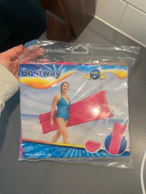 Rosa badmadrass från Bestway - Säljer en rosa badmadrass från Bestway, perfekt för strandhäng och poolen. Madrassen är 183 cm lång och har klassisk rektangulär form med upphöjd kudde. Tillverkad i slitstark plast som tål vatten och sol. Enkel att blåsa upp och ta med sig till stranden.