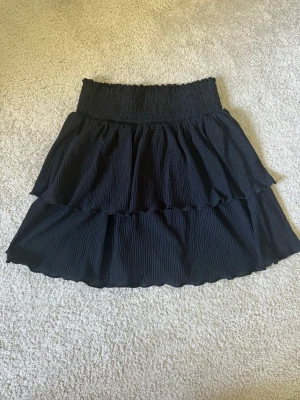 Svart volangkjol från Kappahl - Svart kjol från Kappahl med bred smock i midjan och dubbla volanger. 