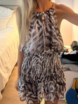Zebra mönstrad Zara klänning - Säljer en snygg kortklänning med brunt och vitt zebramönster. Klänningen har volang nertill, är ärmlös och har en lös passform upptill med smockad midja. Perfekt för dig som gillar trendiga mönster och lätta material.