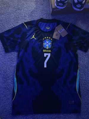 Brasilien Vini Jr Nr7 matchtröja  - Säljer en blå och svart Brasilien matchtröja med nummer 7 och CBF-emblemet på bröstet. Tröjan har gula detaljer, korta ärmar och är tillverkad i ett lätt, andningsbart material som passar perfekt till fotbollsträning eller match.