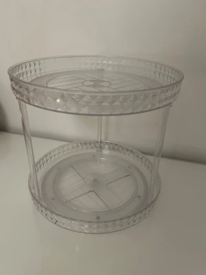 Rund genomskinlig sminkförvaring - Praktisk rund sminkförvaring i genomskinlig plast med diamantmönstrad kant. Två våningar och snurrfunktion gör det enkelt att komma åt allt. 