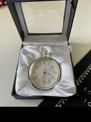 Silverfärgad fickur med skeppmotiv - Stilrent fickur i silverfärg med klassisk rund form och vit urtavla med svarta siffror. Baksidan har en graverad bild av ett segelfartyg. Uret levereras i en elegant ask med vit satinklädsel. Perfekt accessoar för dig som gillar vintagevibbar och detaljer. Pocket Watch