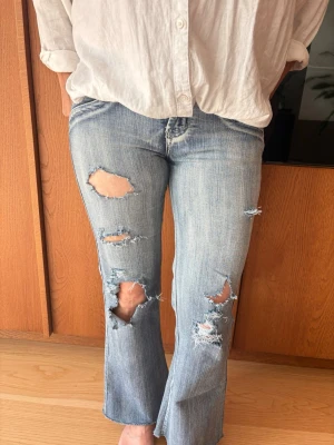 Ping  jeans  ❤️ - Säljer ett par ljusblå bootcut jeans från märket Ping, med flera stora slitningar och hål framtill. Jeansen har klassiska bakfickor med dekorativa sömmar och är tillverkade i denim. Perfekta för en avslappnad och trendig look. Säljer då de är lite för stora på mig, men det finns inga defekter!!