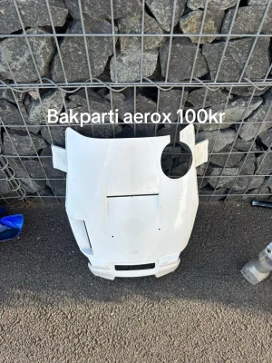 Bakparti till Aerox, vit plast - Bakparti till Yamaha Aerox i vit plast. Delens form är anpassad för att passa bakdelen på en scooter och har utskärningar för lampor och andra detaljer. Perfekt för dig som vill byta ut eller modifiera din moppe.