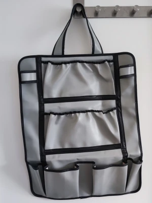 Grå organiseringsväska med fack - Praktisk grå organiseringsväska med flera elastiska fack och svarta kanter. Perfekt att hänga upp med handtaget och förvara småprylar, smink eller accessoarer. Tillverkad i ett slätt syntetmaterial och har smart layout för enkel översikt.