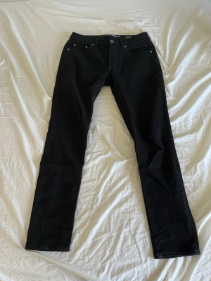 Svarta raka jeans från Dressmann - Säljer ett par svarta jeans med rak passform och klassisk femficksdesign. Jeansen har knappgylf och bälteshällor och är perfekta för en clean och stilren look.