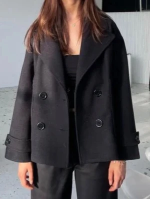 Design by si kappa(aldrig använd!) - Stilren svart skepparkavaj med dubbelknäppning och bred krage. Jackan har lång ärm och en loose passform som ger en avslappnad men ändå klassisk look. Perfekt att slänga över en outfit för extra stilpoäng.