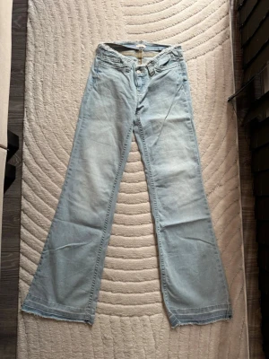 Ljusblå bootcut jeans från Nelly - Säljer ett par ljusblå jeans från Nelly med bootcut passform och råa kanter upptill. Jeansen har klassisk femficksdesign och är gjorda i denim med en skön känsla. Perfekta för dig som gillar en avslappnad och trendig look.