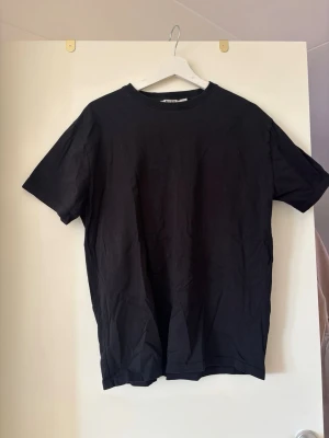 Svart basic t-shirt i bomull - En enkel svart t-shirt med rund hals och korta ärmar. Tillverkad i mjuk bomull och har en normal passform. Perfekt att matcha med jeans eller shorts för en clean look. Lite oversize