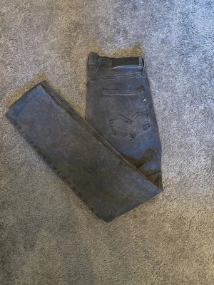 Grå jeans från Replay - Säljer ett par grå jeans från Replay med klassisk femficksmodell och raka ben. Jeansen har en snygg slitning och detaljerad bakficka med Replay-logga. Hör av er vid minsta lilla fråga eller fundering