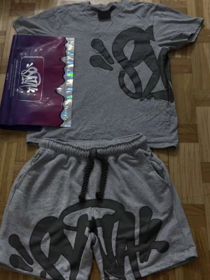 Syna world set - Snygg grå syna world med stort svart grafiskt tryck på framsidan. T-shirten är i mjuk bomull och är perfekt för sommaren. Påse och så finns.