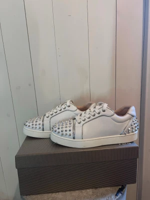 Vita sneakers med silvernitar - Säljer ett par vita sneakers med coola silverfärgade nitar på tå och häl. Skorna har klassisk låg profil, vita snören och en vit sula. Perfekta för dig som vill sticka ut med din stil.