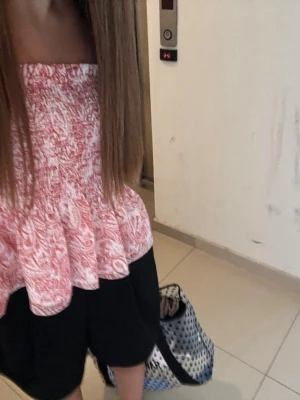 Rödvit ärmlös peplum-topp - Säljer en söt ärmlös topp i rosa och vitt med peplum-modell. Toppen har ett abstrakt mönster och smockad överdel som ger en bekväm passform. Perfekt till sommaren och enkel att styla med shorts eller kjol.