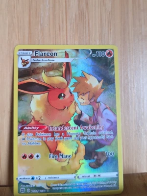 Pokémonkort Flareon TG01/TG30 - Säljer ett Pokémonkort med Flareon och en tränare på framsidan. Kortet har gul ram och färgglad illustration. Det är från serien TG01/TG30 och har text på engelska.