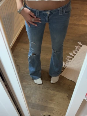 Blå slitna bootcut jeans - Säljer ett par super söta ljusblå bootcut jeans med slitningar för bra pris!