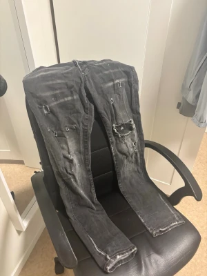 Svarta jeans från Dsquared2 - Säljer ett par svarta jeans från Dsquared2 med slitningar, hål och patchdetaljer. Jeansen har en smal passform och coolt tvättad look. Perfekta för dig som gillar streetstyle och vill sticka ut lite extra. ÄKTA självklart!😁