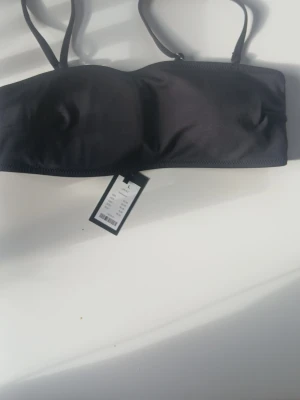 Svart bandeau-bh med avtagbara band - Stilren svart bikini-bh, med avtagbara axelband. Bh:n har slät yta och lätt vadderade kupor för en enkel och bekväm komfort.