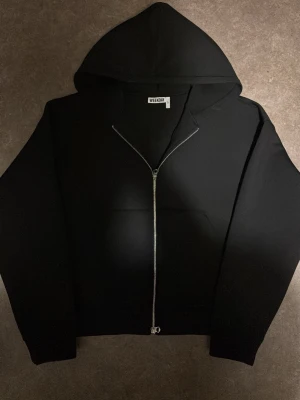 Svart hoodie med dragkedja från Weekday - Säljer en svart hoodie från Weekday i storlek L. Hoodien har dragkedja framtill, huva och en klassisk känguruficka. Perfekt för en chill och stilren look. Materialet är mjukt och bekvämt, passar till det mesta.