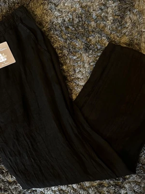 Svarta vida linnebyxor - Säljer ett par svarta linnebyxor i 100% lin. Byxorna har en avslappnad, vid passform och resår i midjan för extra komfort. Perfekta för en chill och stilren look. Tillverkade i Italien.