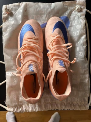Nike Mercurial rosa/blå fotbollsskor - Säljer ett par Nike Mercurial fotbollsskor i en snygg ljusrosa färg med blå detaljer och logga. Skorna har snörning, låg profil och är tillverkade i ett lätt syntetmaterial för bästa bollkontroll och är konstgräs skor. Strl 43. Har använt de 5 gånger men kände de var för små för mina breda fötter. 