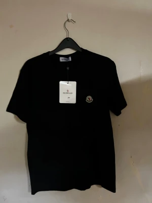Moncler T-shirt  - Snygg svart t-shirt från Moncler med klassisk rund hals och Moncler-logga broderad på bröstet. T-shirten är enkel och stilren, perfekt till jeans eller shorts. Tillverkad i mjuk bomull för en skön känsla.