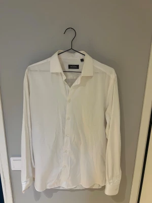 Vit skjorta från Dressmann M helt strykfri - Klassisk vit skjorta från Dressmann i bomullsstretch. Skjortan har lång ärm, knappar framtill och en stilren krage. Perfekt för en clean och enkel look. Helt strykfri.