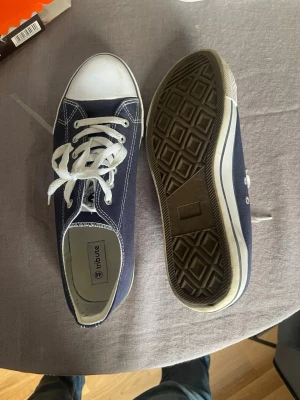 Mörkblå sneakers  - Snygga mörkblåa sneakers från Tribute med vit tå och vita snören. Klassisk låg modell med vit sula och kontrastsömmar. Ovandelen är i canvasmaterial och sulan i gummi. Perfekta för en avslappnad och stilren look. Jätte sköna, rekommenderar