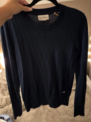 Mörkblå stickad tröja  - Mörkblå stickad tröja från Holly & Whyte med rund halsringning och långa ärmar. Enkel och stilren design som passar perfekt till jeans eller kjol. Tröjan har ribbstickade muddar vid hals, ärmslut och nederkant.