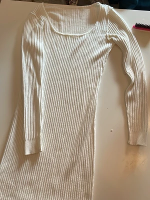 Vit ribbad långärmad klänning - Snygg vit ribbad klänning med lång ärm och rundad urringning. Klänningen har en kroppsnära passform och är tillverkad i ett stretchigt material som ger en bekväm känsla. Perfekt för dig som gillar en enkel men stilren look.