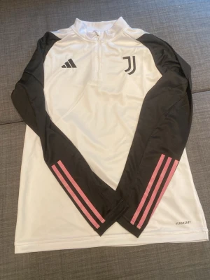 Juventus set - Juventus träningsset från Adidas med långärmad vit tröja och svarta ärmar, dekorerad med rosa ränder och klubbens logga på bröstet. Matchande vita byxor med rosa ränder och Juventus-logga. Tillverkat i lätt och ventilerande material.