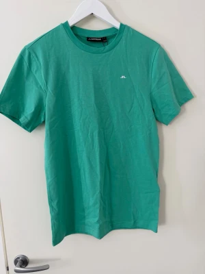Grön t-shirt från J.Lindeberg - Snygg grön t-shirt från J.Lindeberg med diskret logga på bröstet. Klassisk rund halsringning och korta ärmar. Tillverkad i mjuk bomull som känns skön mot huden. Perfekt till jeans eller shorts för en clean och enkel look!😌