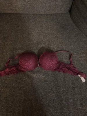 Vinröd push-up bh med spetsdetaljer - Snygg vinröd push-up bh med vadderade kupor och fina spetsdetaljer över hela bh:n. Justerbara axelband och hakknäppning bak. Perfekt för dig som vill ha en bh med både stöd och en feminin look.