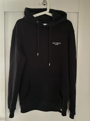 Svart hoodie från Les Deux - Snygg oanvänd svart hoodie från Les Deux med minimalistisk vit logga på bröstet. Klassisk modell med huva, snören i metall. En kvalitets hoodie..