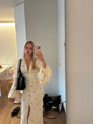 Vit långklänning med blommigt mönster - Lång klänning från adoore. Köpt innan sommaren och använd 3 gånger på semester. Superfint skick utom en mycket liten fläck som säkerligen går bort i tvätten, har själv ej testat. Storlek 32 (xxs). Säljer för 1200 nypris: 1695