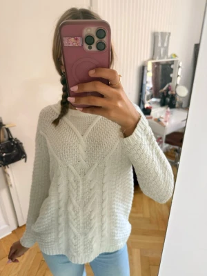 Vit kabelstickad tröja - Säljer en vit kabelstickad tröja med rund hals och långa ärmar. Tröjan har ett snyggt mönster med grova flätor framtill och ribbade muddar. ✨✨