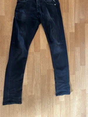 Svarta replay grover jeans - Säljer ett par svarta replay grover jeans med klassisk femficksdesign och dragkedja. Jeansen har smal passform och raka ben, perfekta till en avslappnad stil. Materialet ser ut att vara en bomullsblandning med lite stretch för extra komfort. Strl w29 L32
