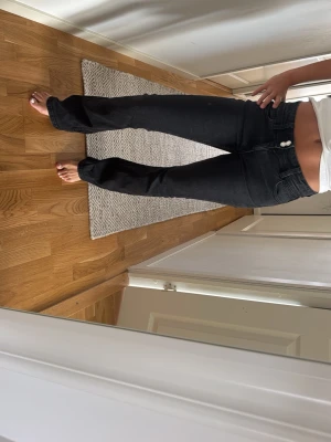 Svarta bootcut jeans med medelhög midja - Snygga svarta bootcut jeans med låg midja och raka ben. Jeansen har klassisk femficksdesign och stängs med två knappar framtill. Perfekta för dig som gillar en stilren och trendig look.