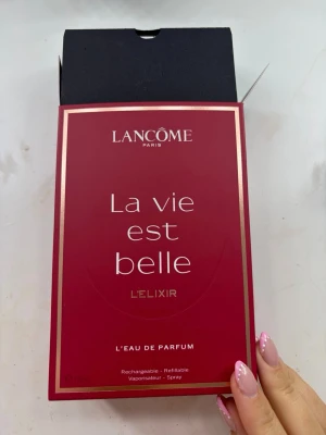 Lancôme La Vie Est Belle L'Élixir parfym - En lyxig parfym från Lancôme, La Vie Est Belle L'Élixir, i en elegant glasflaska med rödrosa doftvätska. Flaskan har en snygg silverdetalj vid halsen och en transparent fyrkantig kork. Kommer i en stilren vinröd kartong med gulddetaljer.