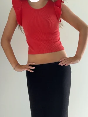 Röd ribbad croppad topp med volang - Snygg röd croppad topp med ribbad struktur och volangdetaljer vid axlarna. Toppen är ärmlös och har en rund halsringning. Perfekt för dig som vill ha en trendig och bekväm look.