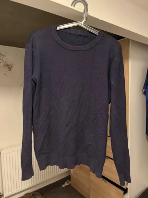 Mörkblå basic tröja - En enkel och stilren mörkblå tröja med rund halsringning och långa ärmar. Tröjan har ribbade muddar vid ärmslut och nederkant. Perfekt att matcha med jeans eller kjol för en clean look.