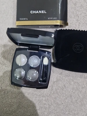 Chanel ögonskuggspalett i silvertoner - Snygg ögonskuggspalett från Chanel med fyra skimrande nyanser i silver, grått och taupe. Kommer i en elegant svart dosa med spegel och applikator samt tillhörande sammetsfodral. Perfekt för att skapa olika ögonlooks med metallic finish.