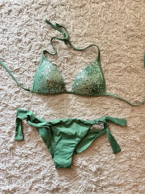 Calzedonia Bikini - Snygg grön bikini med trekantsöverdel dekorerad med glittriga paljetter och knyt i nacken. Underdelen har knyt i sidorna för justerbar passform. Perfekt för sommarens strandhäng eller poolparty. Från Calzedonia. Säljs pga för liten. Så den är bara testad