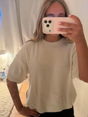 Vit stickad tröja med kort ärm - Mysig vit stickad tröja med korta ärmar och rund hals. Tröjan har en avslappnad passform och ribbade kanter vid hals och nederkant. Perfekt att styla med jeans eller kjol för en enkel och clean look.