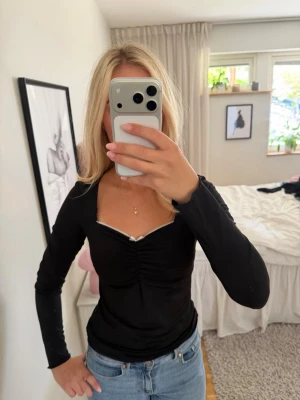 Svart långärmad topp med v-ringning - Snygg svart långärmad topp med markerad v-ringning och lätt rynkning framtill. Toppen har en figurnära passform och är perfekt att styla med jeans eller kjol. Materialet känns mjukt och stretchigt.