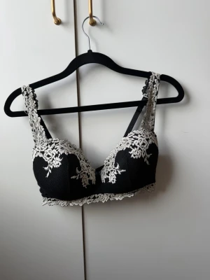 Intimissimi bh - Snygg svart bh med breda axelband och vacker vit spetsbrodyr över kuporna och banden. Bh:n har vadderade kupor och spetskant nedtill som ger en romantisk känsla. Materialet är mjukt och stretchigt för extra komfort.