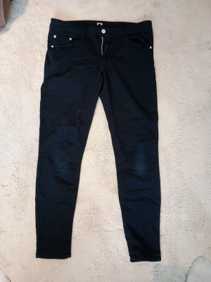 Svarta jeans med fickor - Säljer ett par svarta jeans med en klassisk femficksdesign. De har knapp och dragkedja framtill samt bakfickor. Materialet är stretchigt och mjukt, vilket gör dem bekväma och lätta att röra sig i. Perfekta till en avslappnad look.