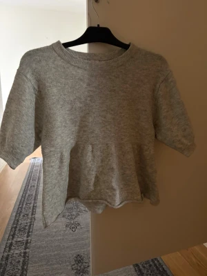 Grå stickad topp från Nelly - Mysig grå stickad topp från Nelly i storlek XS. Toppen har rund halsringning och korta ärmar, perfekt för lager på lager eller till ett par jeans. Enkel och stilren design som passar till många olika looks.