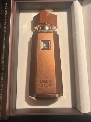 Parfymflaska Liquid Brun brun 100ml - 100ml kvar Snygg parfymflaska i metallisk brun färg med gulddetaljer och geometrisk form. Flaskan har en unik, mångkantig kork och elegant design med texten LIQUID BRUN på framsidan. Perfekt för dig som gillar exklusiva och stilrena dofter.