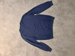 Massimo Dutti tröja - En stilren blå stickad tröja med rund hals och diskret strukturmönster. Tröjan har långa ärmar och ribbade muddar vid ärmslut och nederkant. Perfekt att matcha med jeans eller chinos för en avslappnad look.